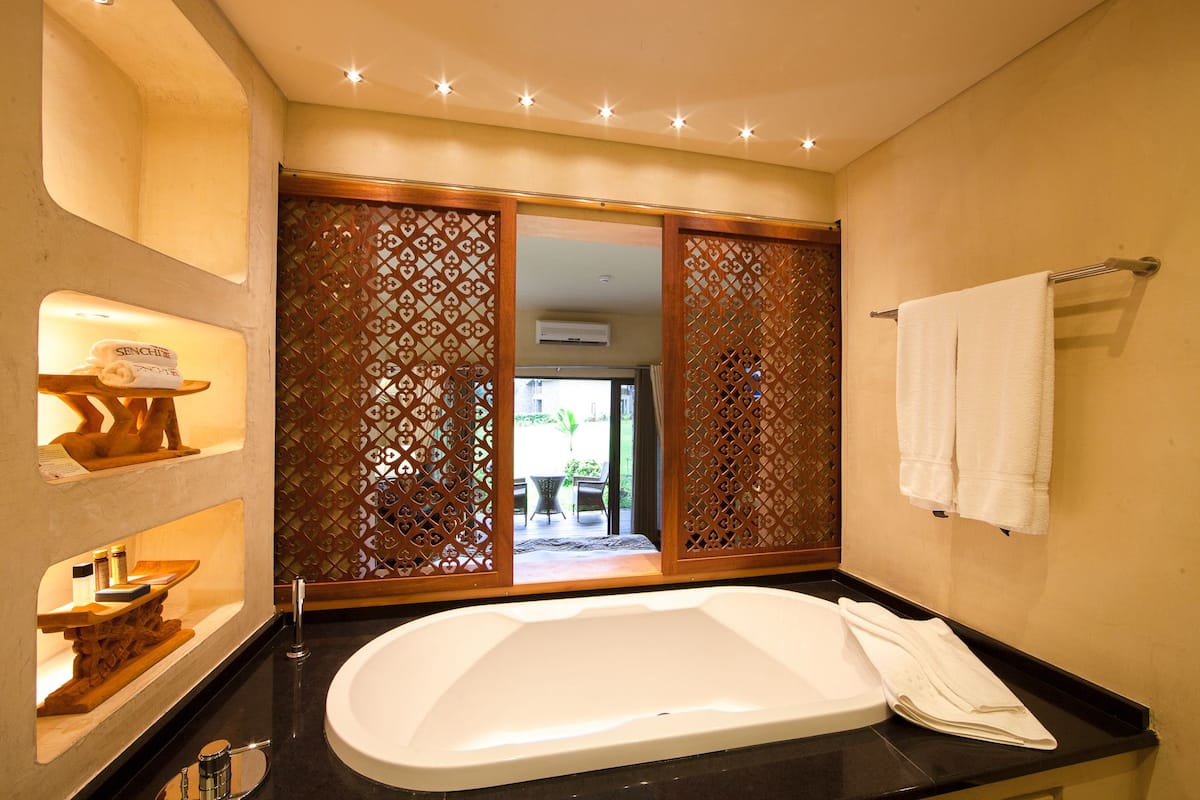A bathroom with a large bathtub, a wooden partition, and a towel rack.