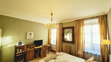 Una habitación de hotel con una cama, un escritorio con una silla, una televisión y un candelabro.