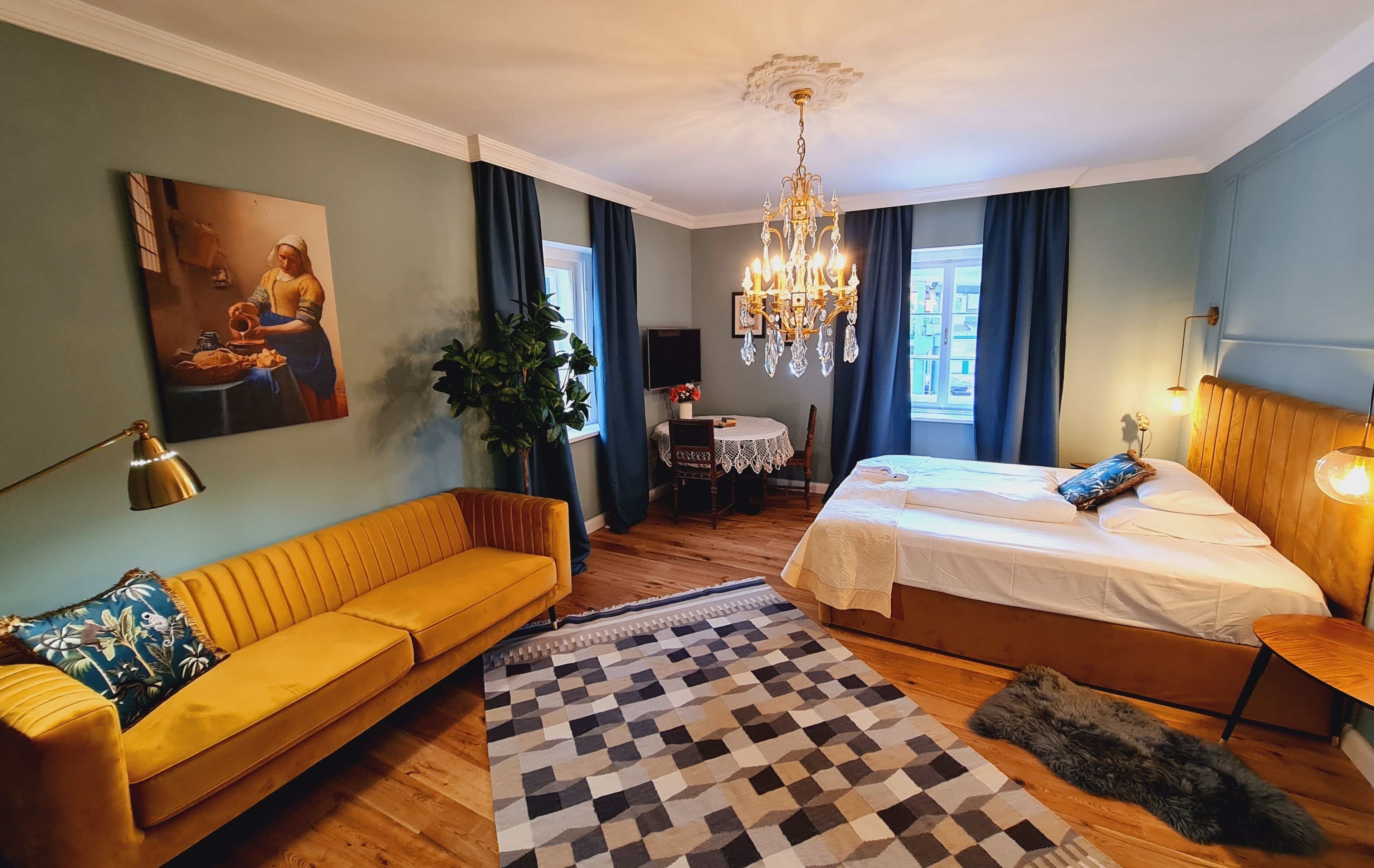 Et hotelværelse med seng, sofa, spisebord, en lysekrone og et billede på væggen.