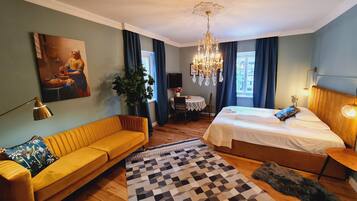 Et hotelværelse med seng, sofa, spisebord, en lysekrone og et billede på væggen.