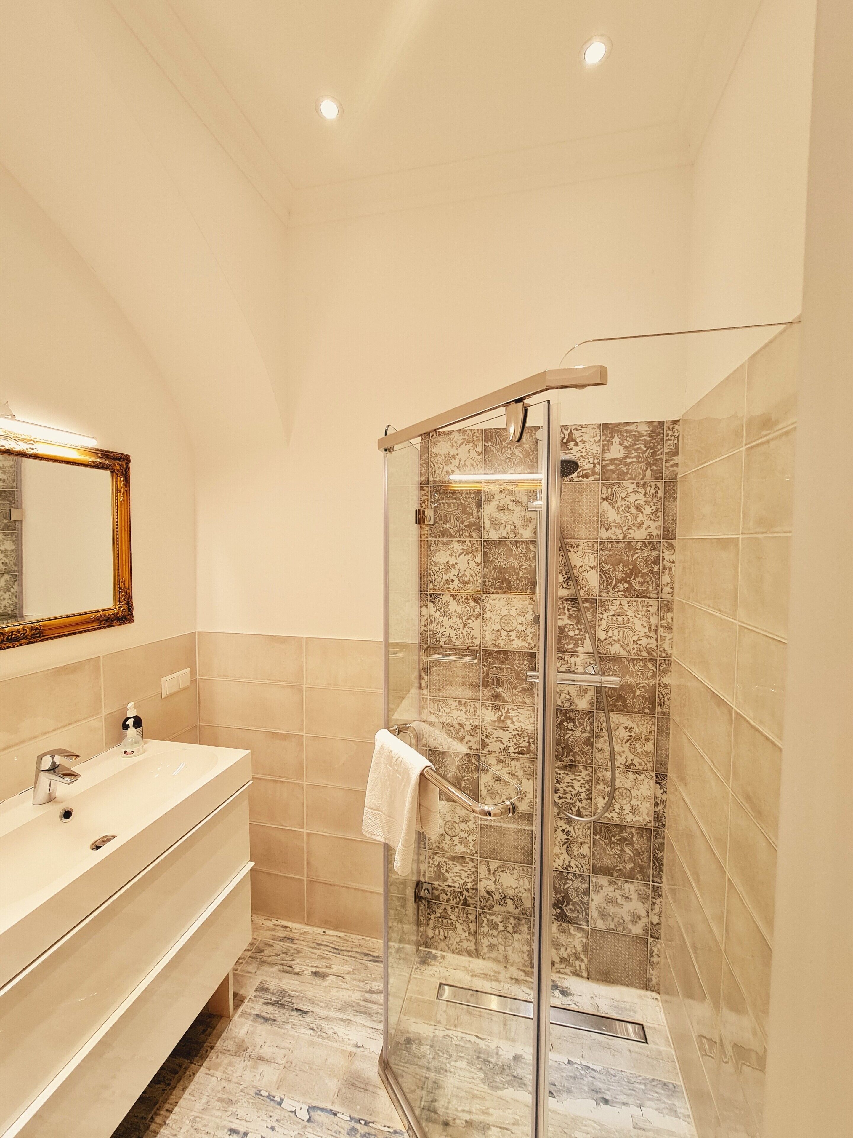 A modern bathroom with a glass-enclosed shower, a vanity with a mirror, and patterned tiles.