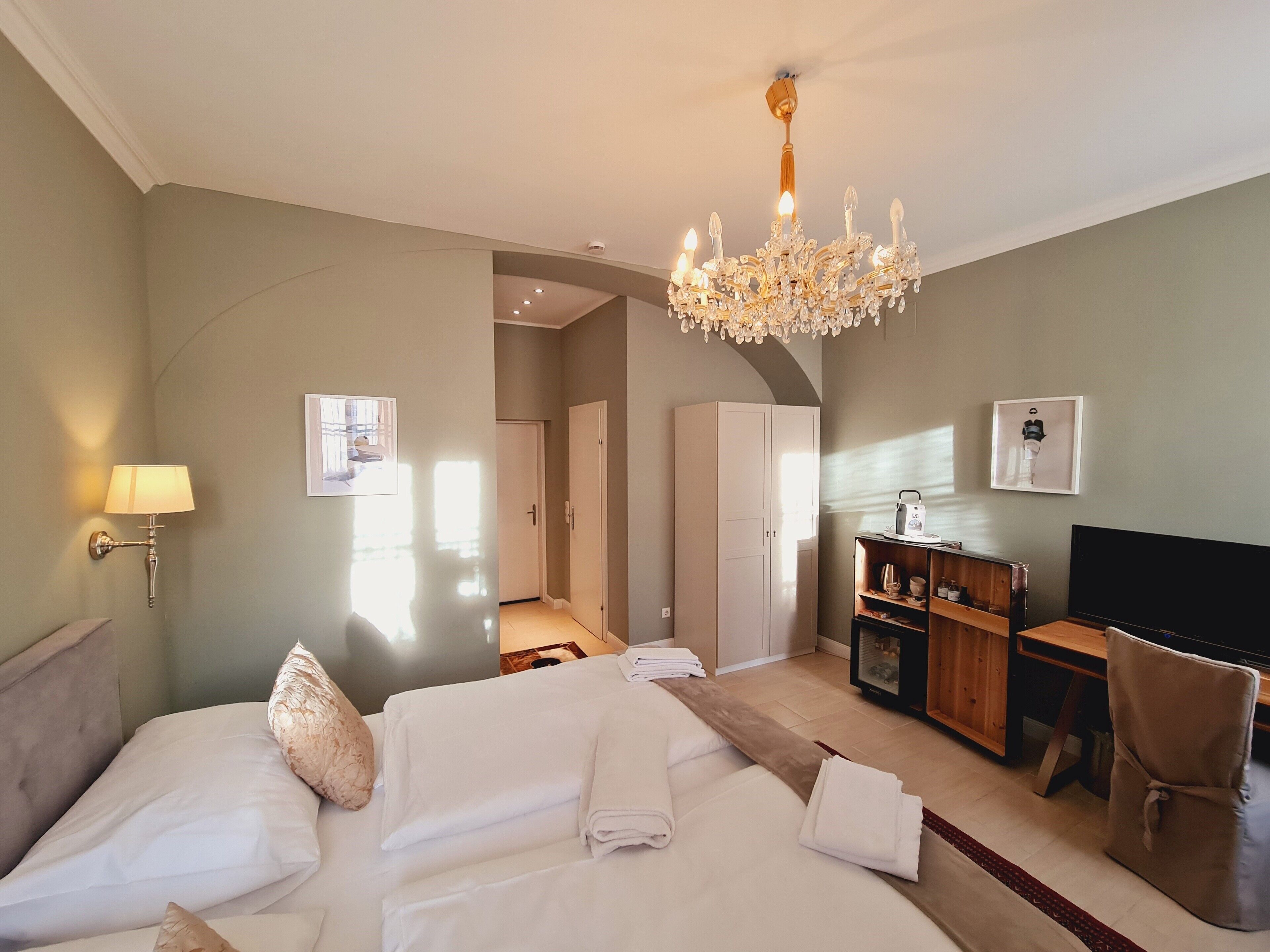 A hotel room with a bed, a desk, a chair, a television, and a chandelier.