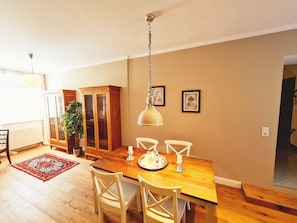 A dining area with a wooden table, white chairs, a hanging lamp, a cabinet, and a potted plant. - Gewerkenschlössl Zeilinger (Knittelfeld)