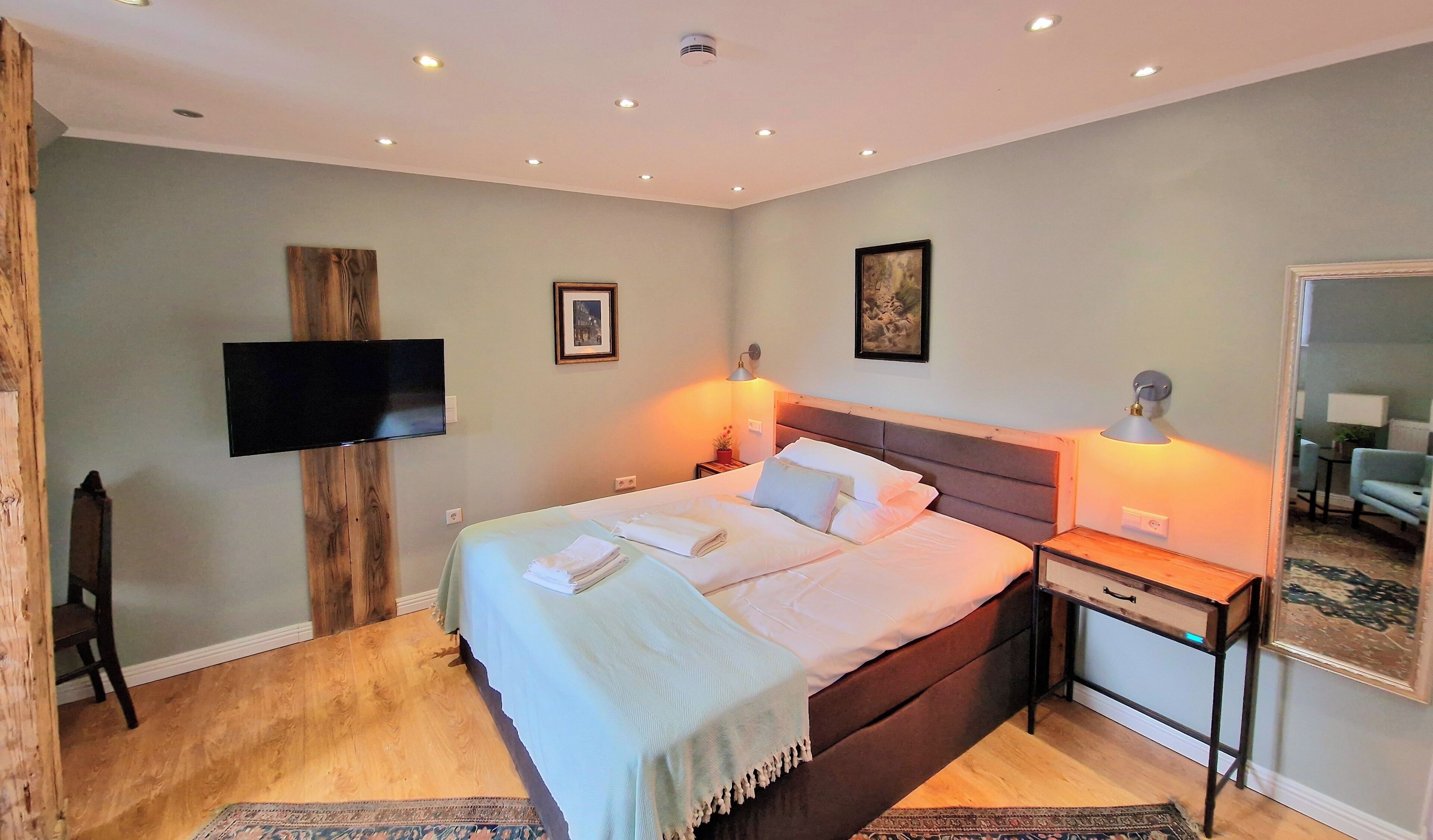A hotel room with a bed, bedside lamps, a flat-screen TV, and a wooden accent wall.