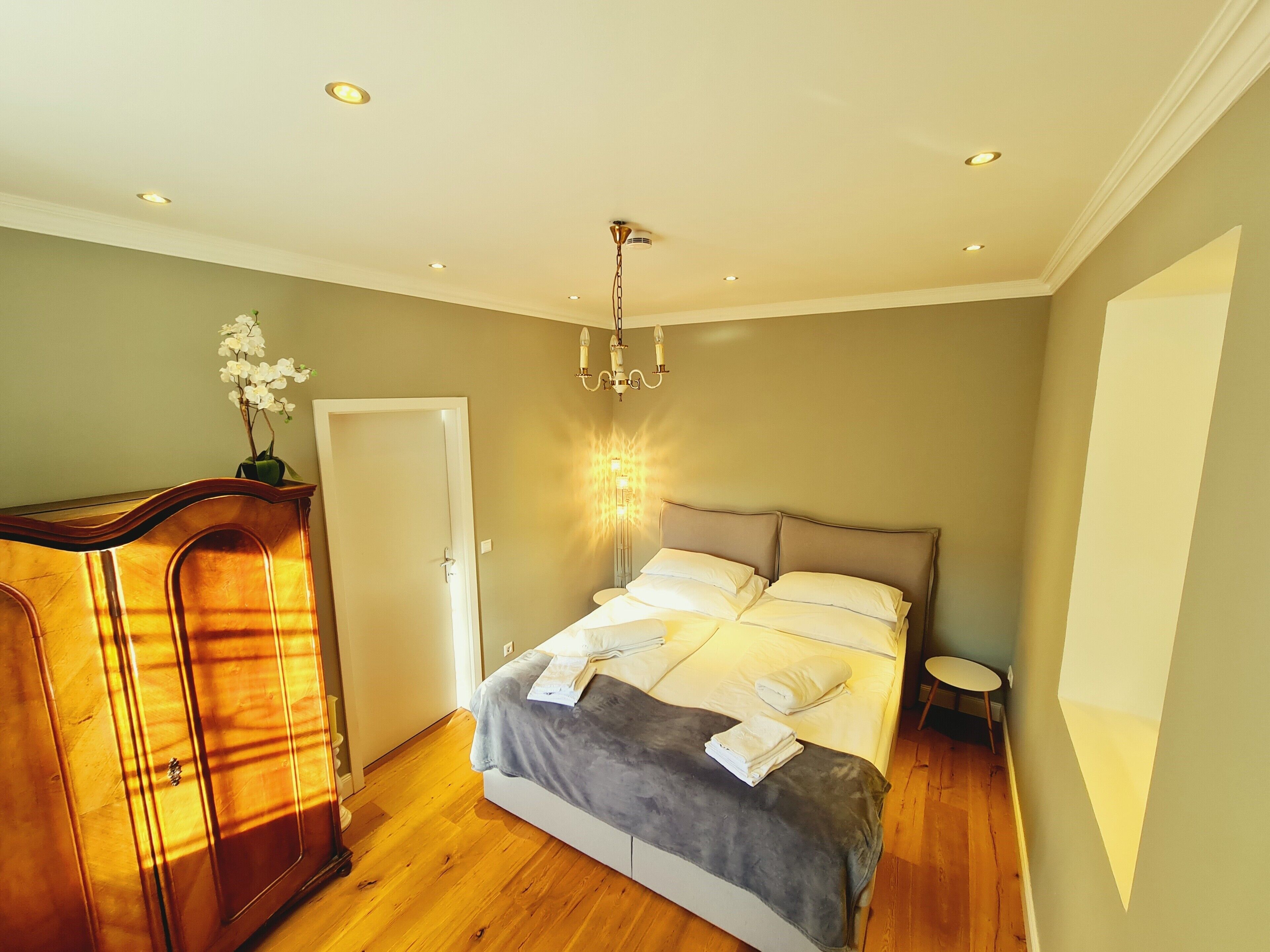 A bedroom with a bed, a dresser, a chandelier, and a small table.