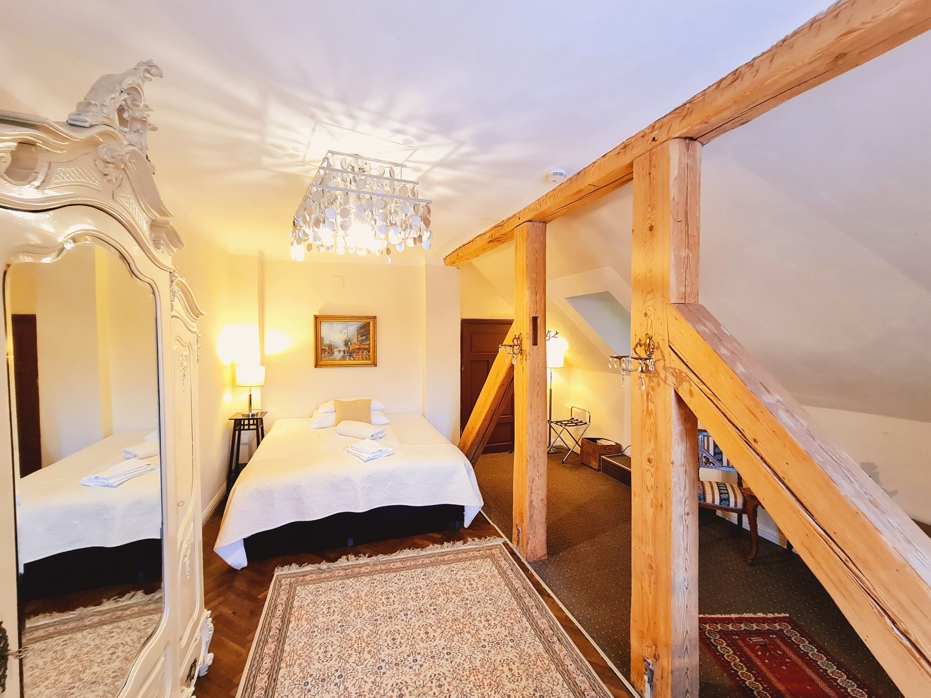 A bedroom with two beds, a chandelier, a painting, and a wooden staircase.
