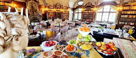 Une bibliothèque agrémentée de boiseries décoratives, de rayonnages et d’un coin repas où l’on sert des fruits et des pâtisseries.