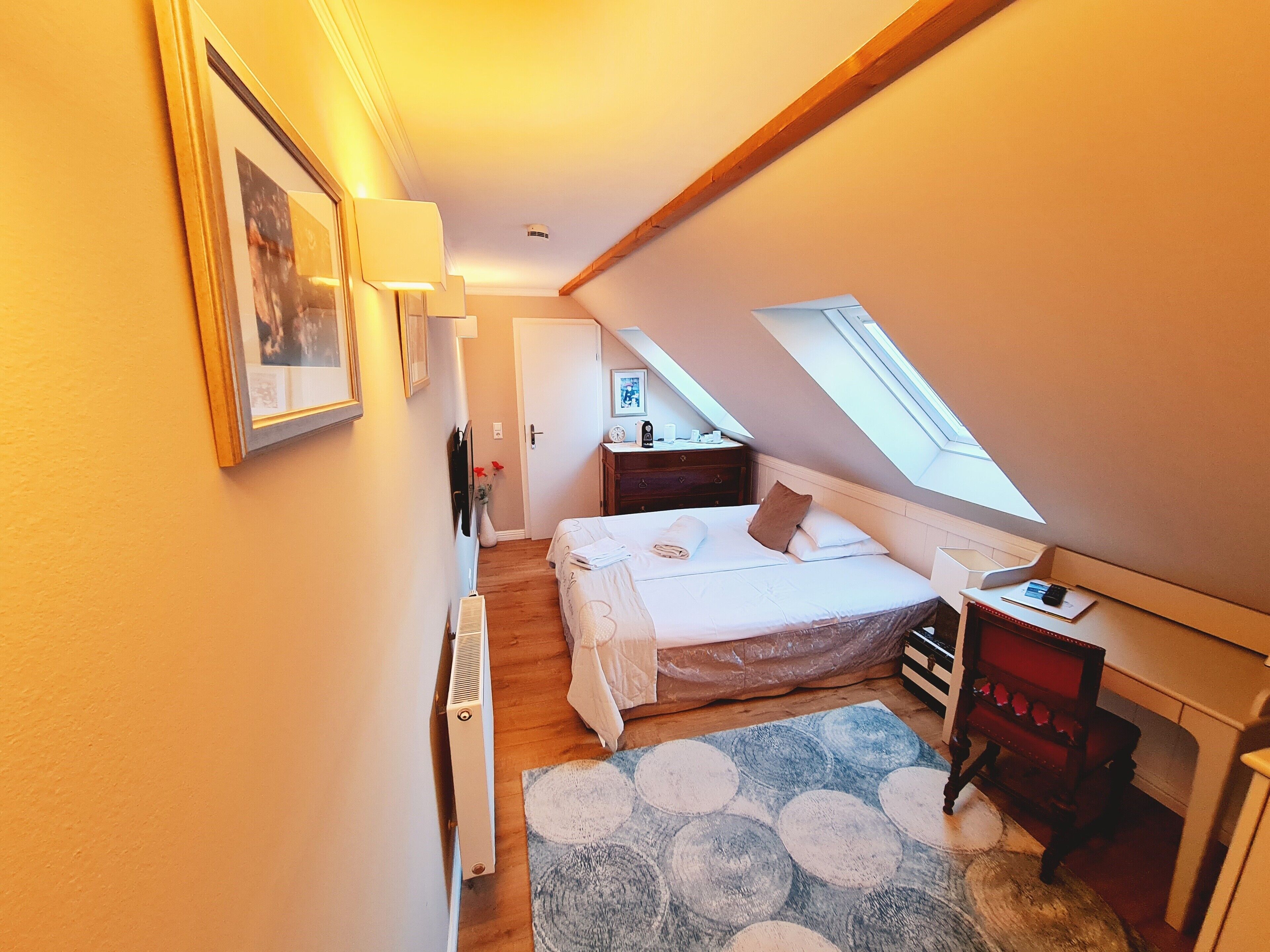 A narrow, well-lit room with a bed, a desk, and a radiator.