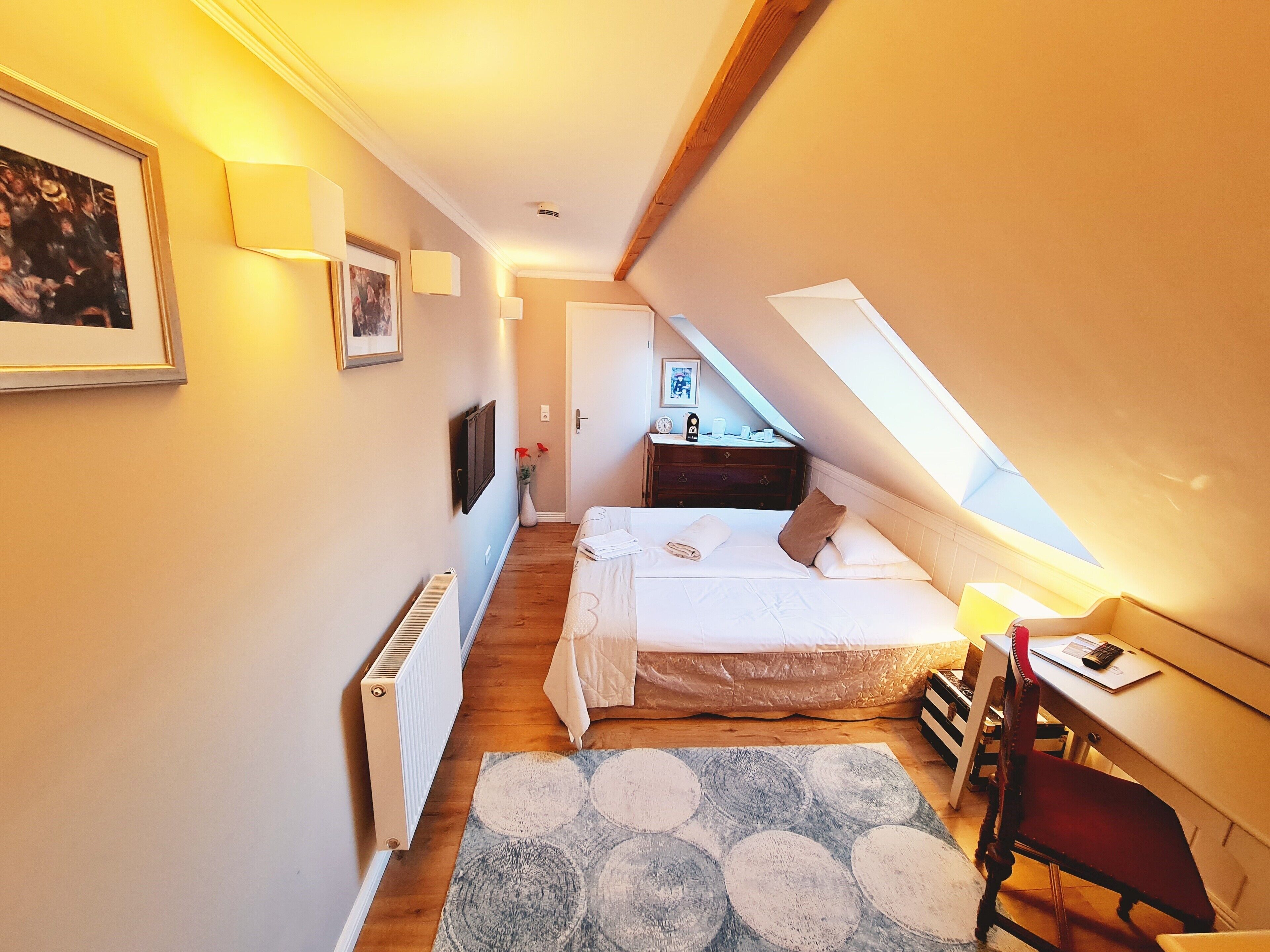 A bedroom with a bed, a desk, a chair, a radiator, and a window.