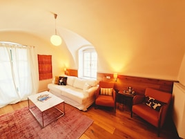 Uma sala de estar aconchegante com um sofá branco, uma mesinha e duas cadeiras. Há duas luminárias na parede e uma luminária no teto.