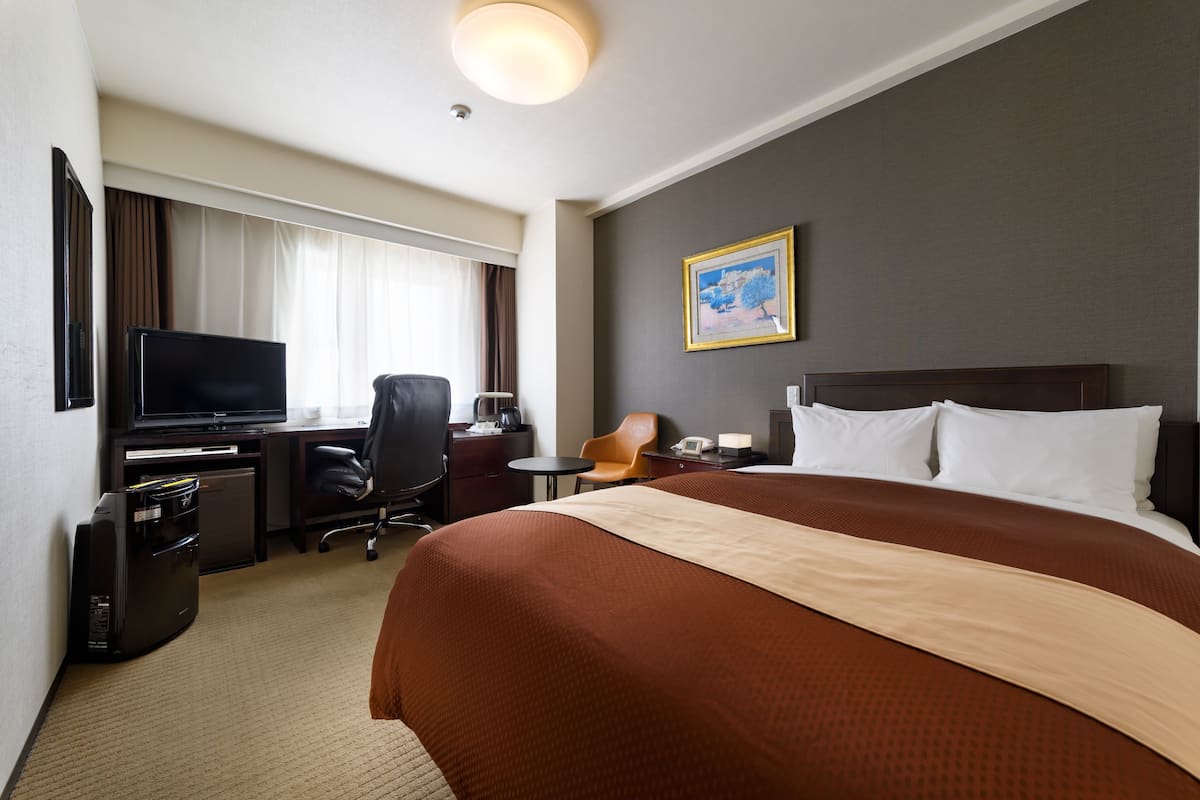 Habitación de hotel con una cama grande, un escritorio con televisor, una silla y una mesita.