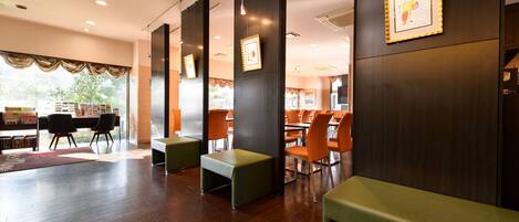A modern interior with wooden floors, green and orange seating, and framed artwork on the walls.