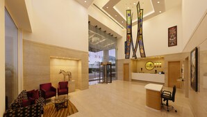 A hotel lobby with a reception desk, seating area, and a glass wall offering a view of the city. - Lemon Tree Hotel Gachibowli Hyderabad (Hyderabad)