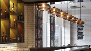 A bar area with wooden shelves, hanging pendant lights, and bar stools. - Lemon Tree Hotel Gachibowli Hyderabad (Hyderabad)