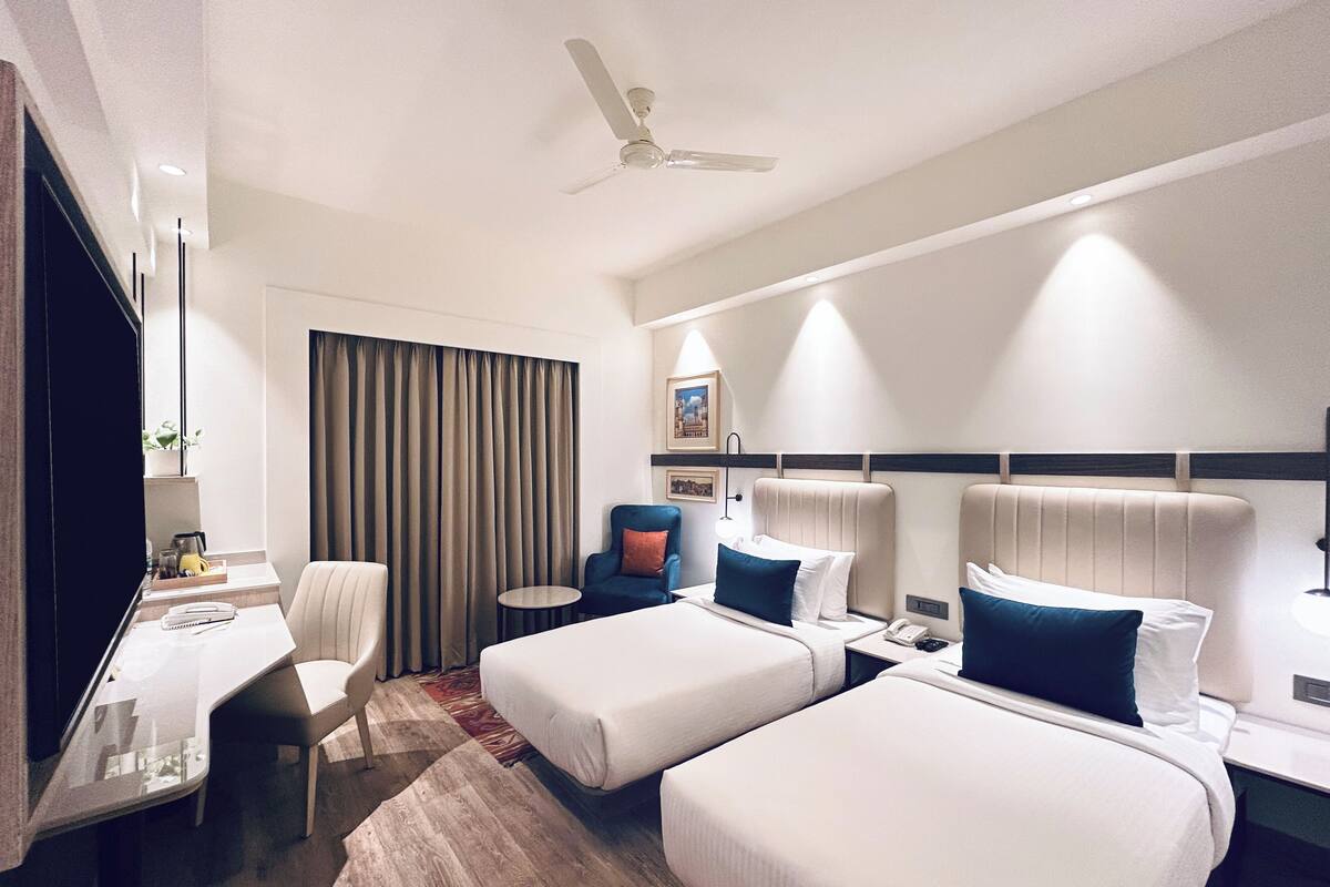Ein Hotelzimmer mit zwei Betten, einem Schreibtisch, einem Stuhl, einem kleinen Tisch und einem Deckenventilator.