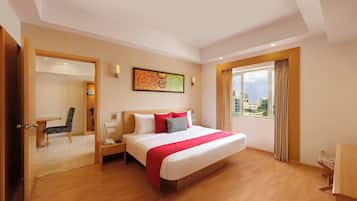 A hotel room with a large bed, a desk, a chair, a window with curtains, a painting on the wall, and a TV.
