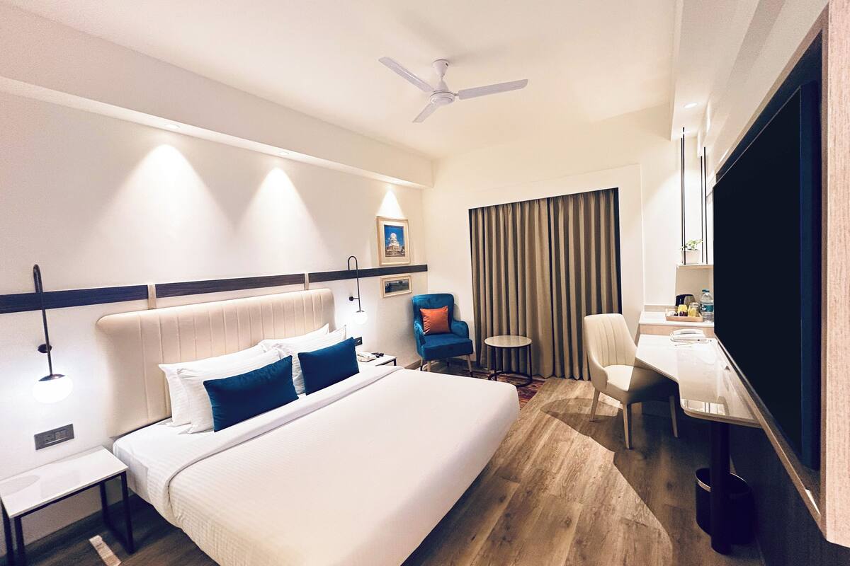 Ein Hotelzimmer mit einem großen Bett, einem Schreibtisch, einem Stuhl, einem Deckenventilator und einem Fernseher.