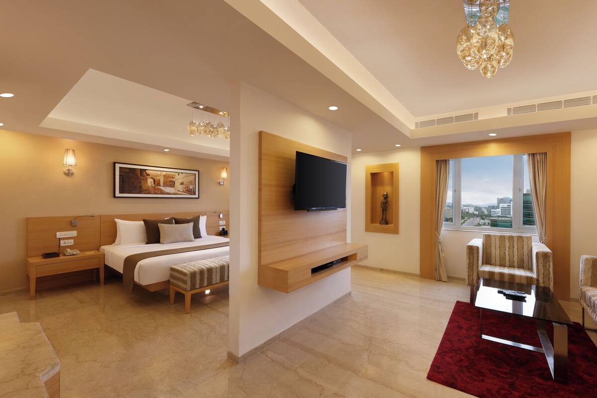 Ein Hotelzimmer mit Bett, Nachttisch, Lampe, Fernseher, Sitzecke und Blick auf die Stadt.