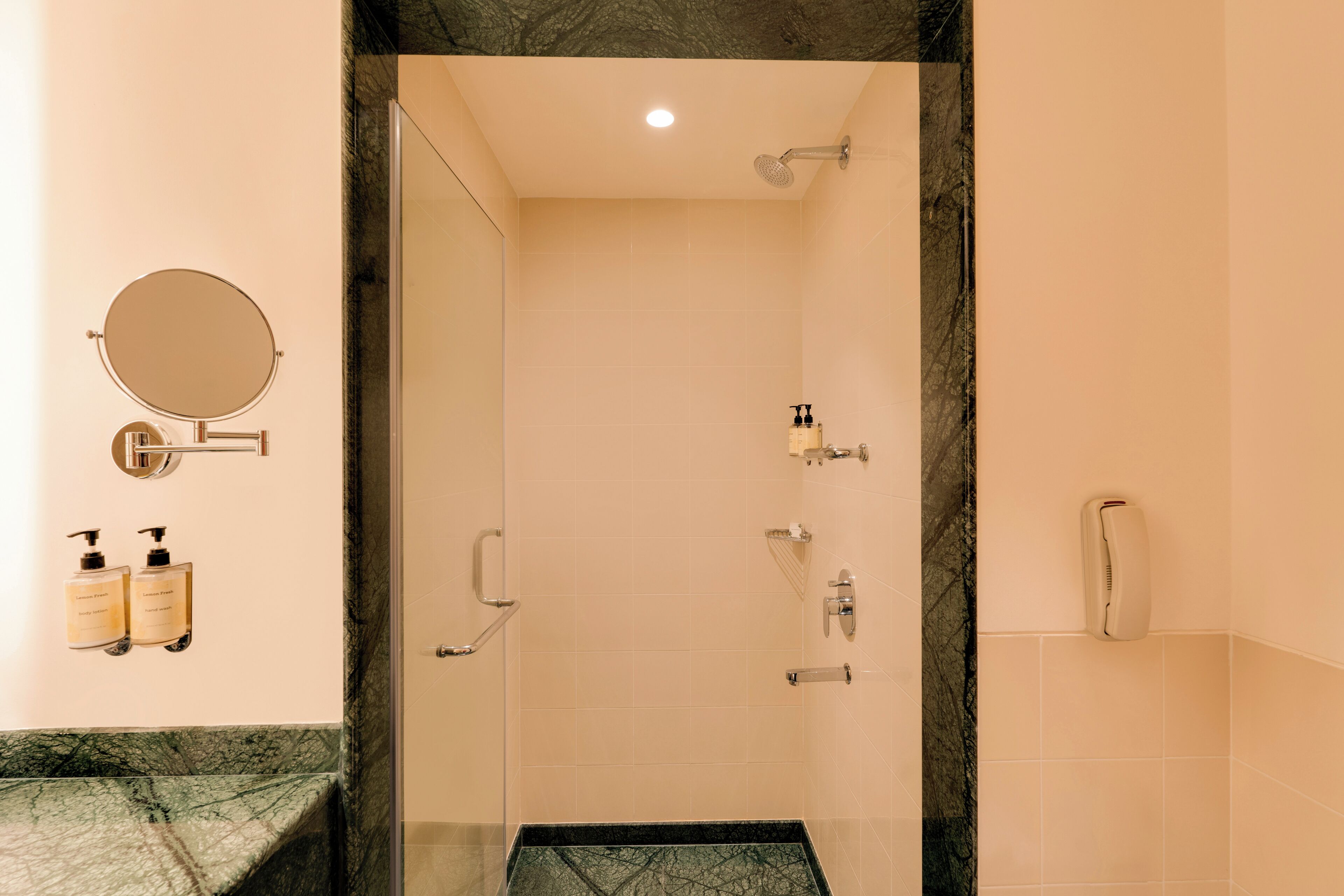 A modern bathroom with a glass-enclosed shower, a round mirror, and two hand soap dispensers on the wall.