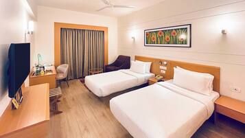 A hotel room with two beds, a desk, a chair, a television, and a ceiling fan.