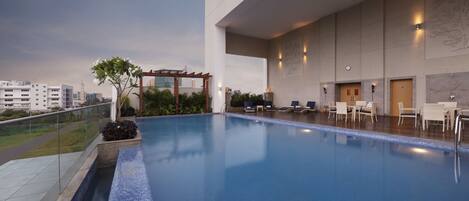 A rooftop pool with lounge chairs and a pergola, surrounded by a cityscape.