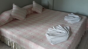 A neatly made bed with a pink checkered bedspread, two pillows, and two folded towels. - Pattara House (Koh Samui)