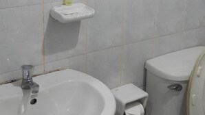 A bathroom with a white sink, a mirror with a red frame, a toilet, and a small shelf with a bottle. - Pattara House (Koh Samui)