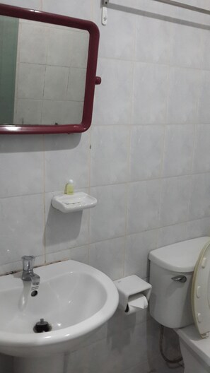 A bathroom with a white sink, a mirror with a red frame, a toilet, and a small shelf with a bottle.