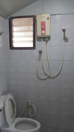 A bathroom with a toilet, a window, and a shower unit.