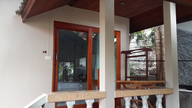A covered porch with a wooden railing, a tiled floor, and a door with a glass panel. - Pattara House (Koh Samui)