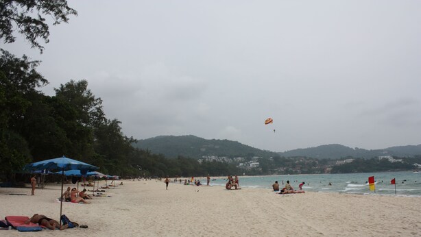 Une plage avec des parasols, des gens et un drapeau.