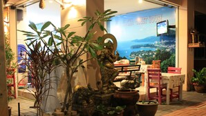 Un restaurant offrant une vue sur une ville côtière, agrémenté de plantes en pot et orné d’une statue de Bouddha.