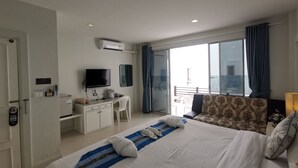 Une chambre d’hôtel avec un lit, un bureau avec une télévision, une fenêtre avec des rideaux et un balcon.