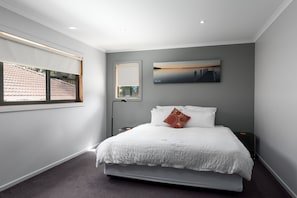 A modern bedroom with a bed, a nightstand, a lamp, and a painting on the wall. - The Edgewater Bed & Breakfast (Sanctuary Point)