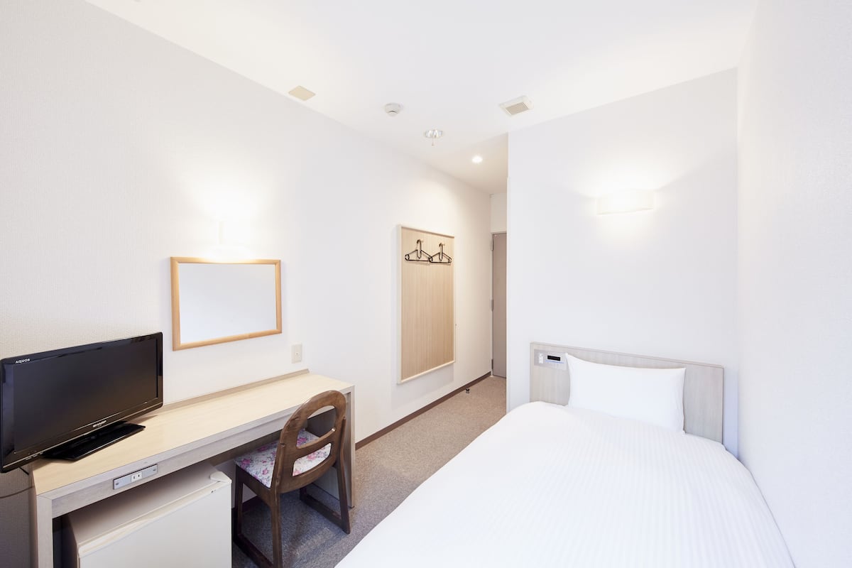 Une chambre d’hôtel comprenant un lit, un bureau avec une télévision, une chaise, une armoire et un luminaire fixé au mur.