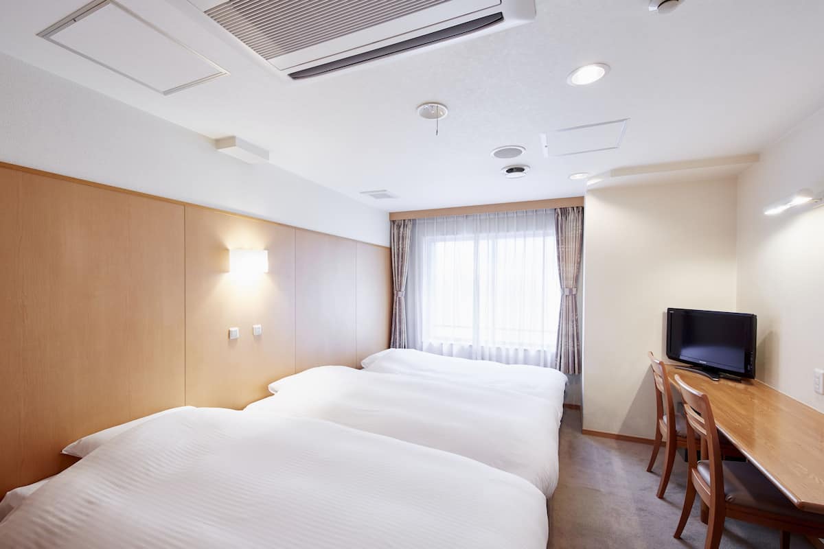 Une chambre d’hôtel avec deux lits, un bureau en bois avec une télévision et une fenêtre avec des rideaux.