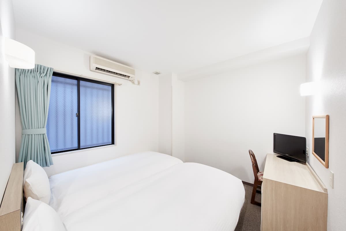 Une chambre d’hôtel avec un grand lit, un bureau avec une télévision, un appareil de climatisation et une fenêtre avec des rideaux.