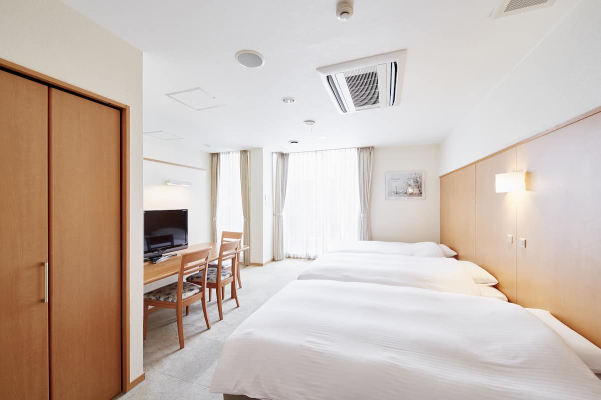 Une chambre d’hôtel avec deux lits, un bureau avec une chaise, une télévision et une armoire.