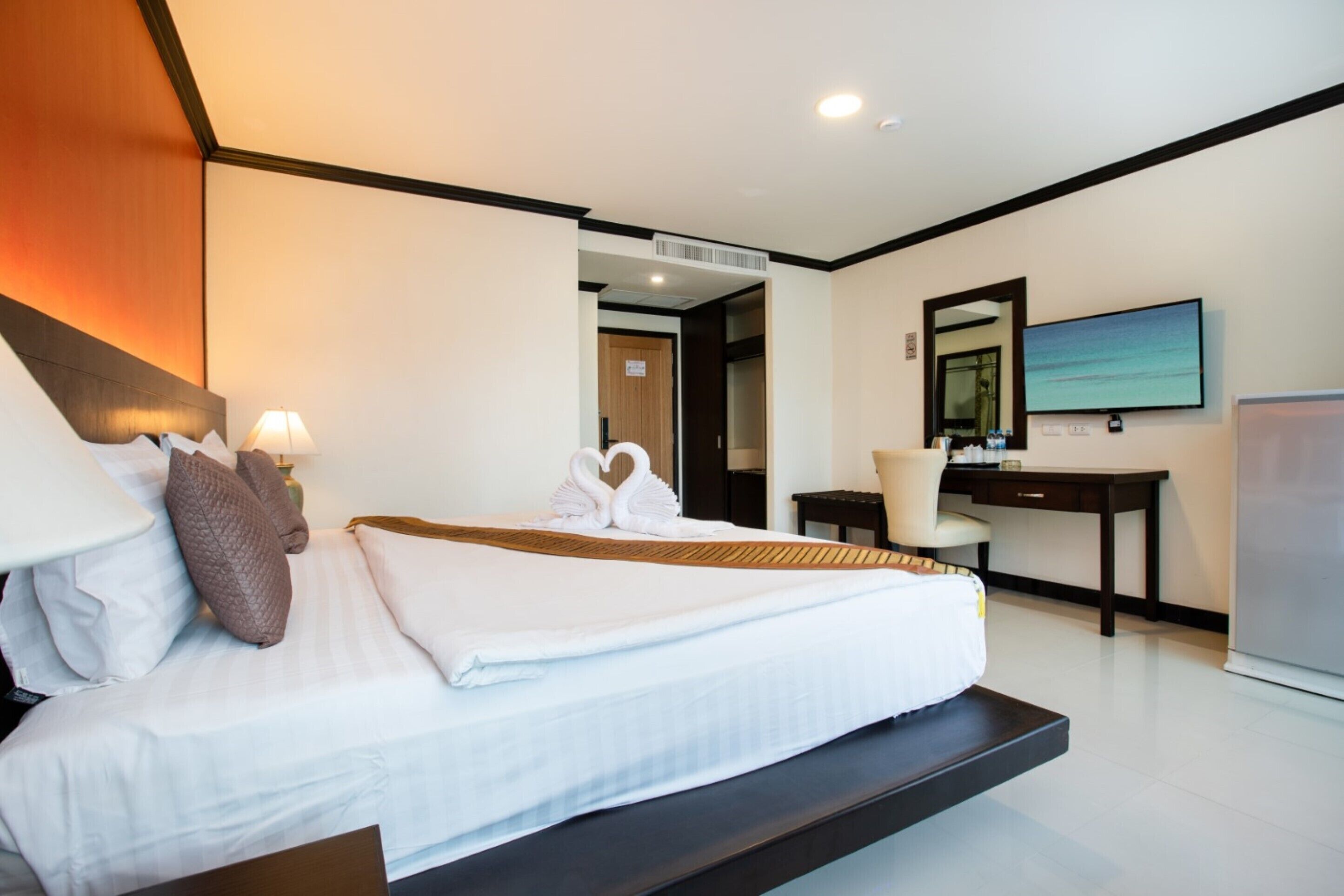 A modern hotel room with a large bed, a desk, a chair, a television, and a bathroom visible through an open door.