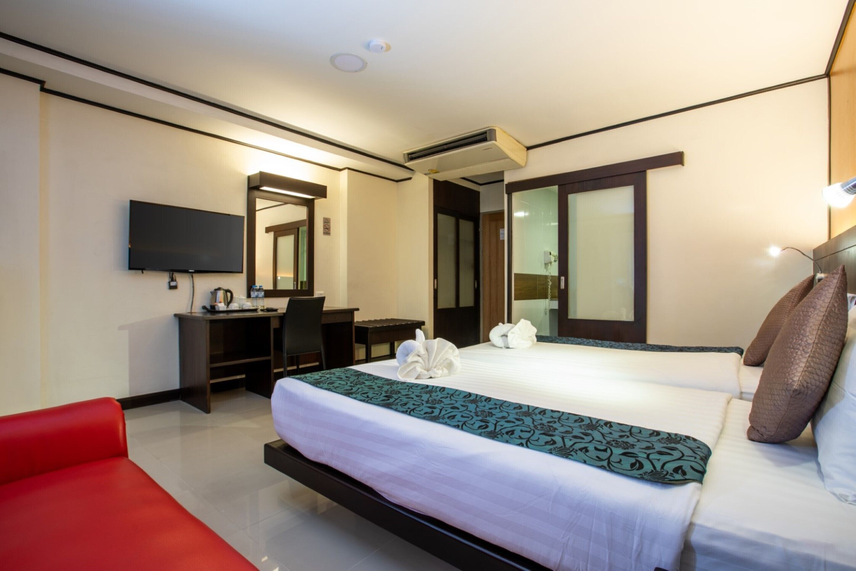 A hotel room with a bed, a desk, a chair, a TV, and a red couch.