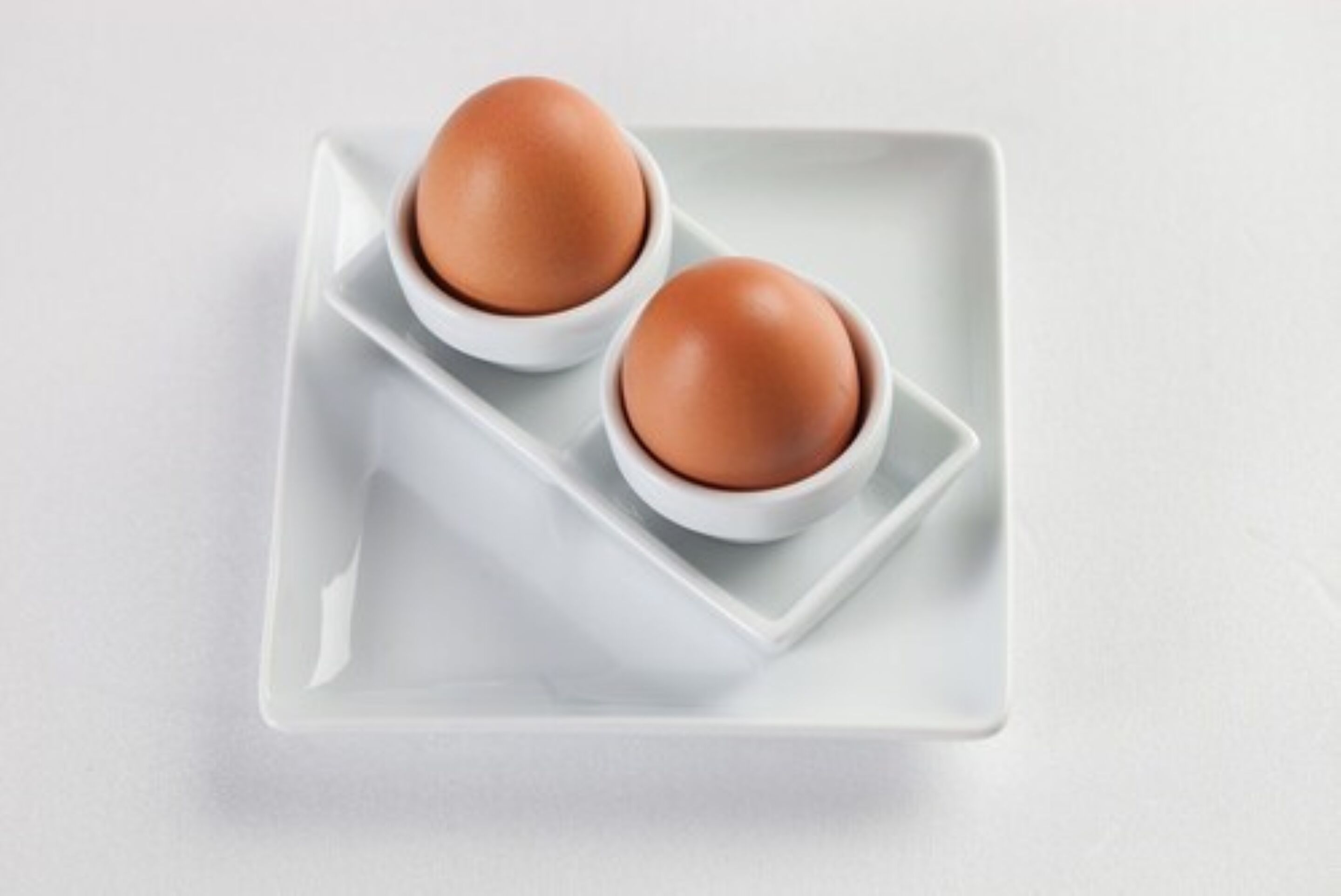Deux œufs bruns dans des bols blancs, posés sur une assiette carrée blanche.