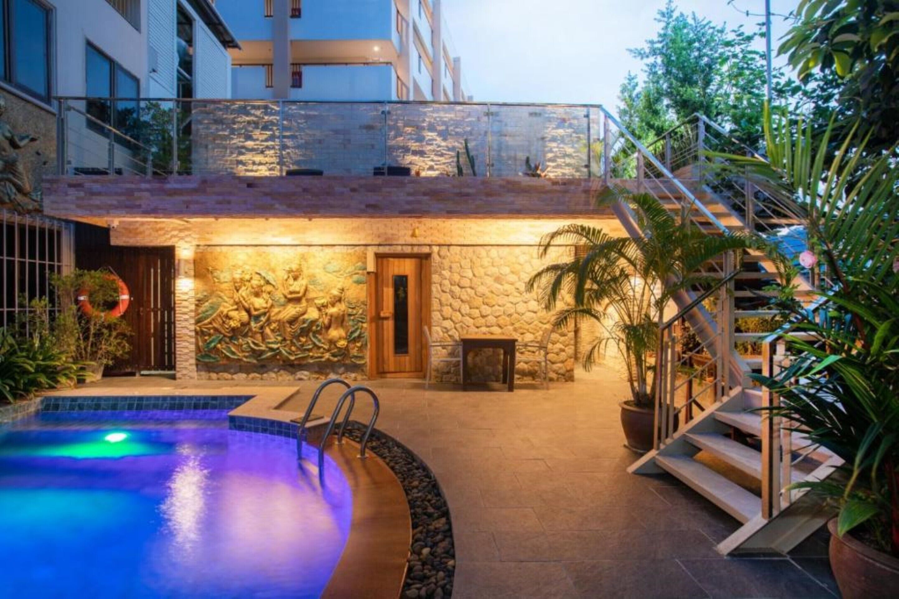 A swimming pool with a stone wall and a wooden door, surrounded by potted plants and a staircase.