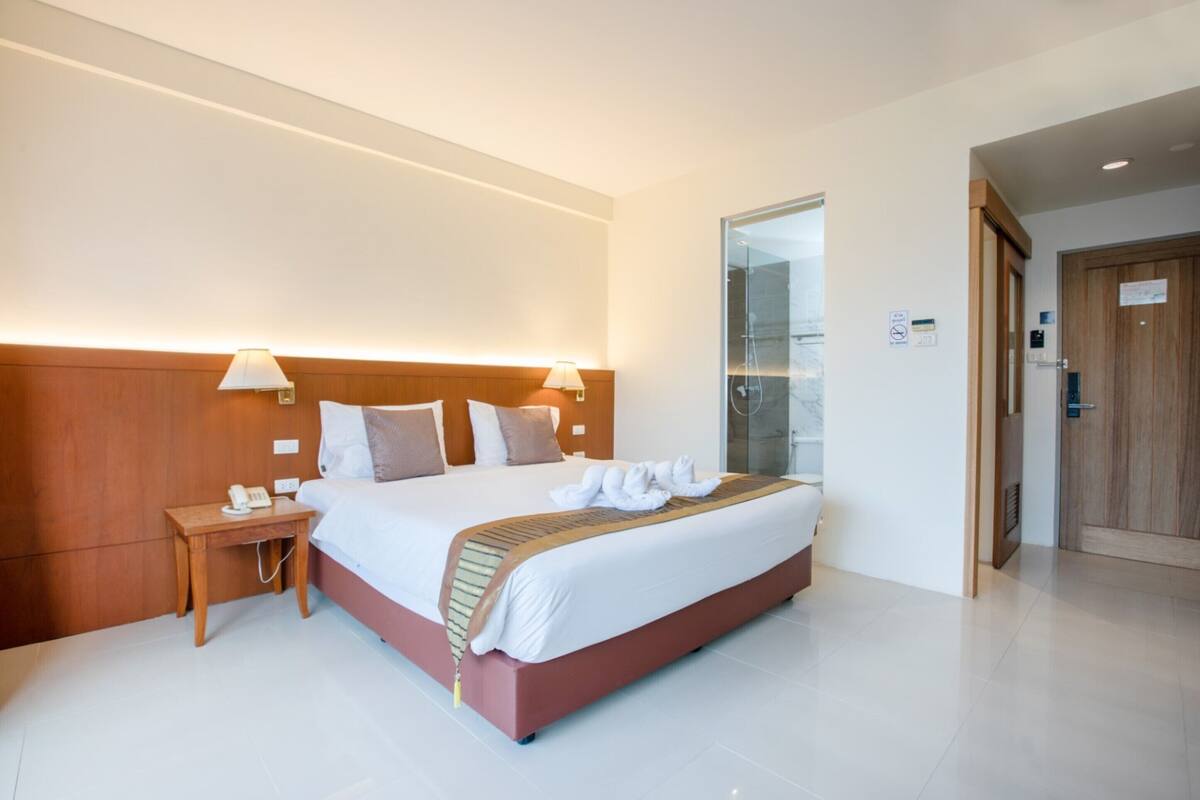 A modern hotel room with a large bed, bedside lamps, a wooden headboard, and a glass shower enclosure.
