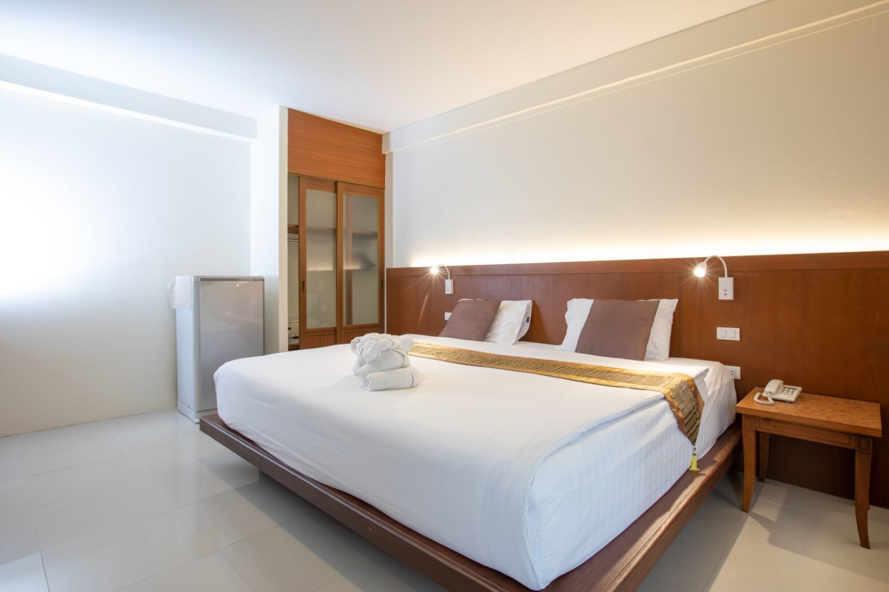 A modern hotel room with a large bed, wooden headboard, bedside table with a phone, and a small desk with a lamp.