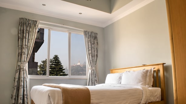 Un dormitorio con cama de madera, una ventana con cortinas y vista a un árbol afuera.