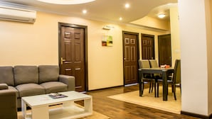 Sala de estar con sofá, mesa de centro y comedor con sillas. Hay dos puertas y un equipo de aire acondicionado en la pared.