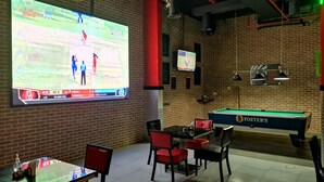 A billiards room with a pool table, red chairs, a television displaying a cricket match, and a brick wall. - Fortune Hotel Deira (Dubai)