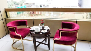 A balcony with two red velvet chairs, a small round table with white teapots and cups, and a potted plant with red flowers. - Fortune Hotel Deira (Dubai)