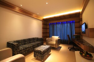 Uma sala de estar moderna com sofá, poltrona, banquinho e uma escrivaninha com computador.