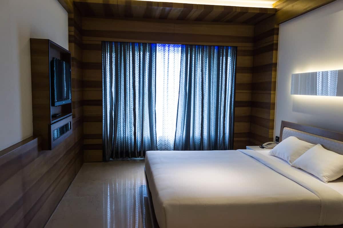 Habitación de hotel con una cama grande, un televisor en la pared y una ventana con cortinas.